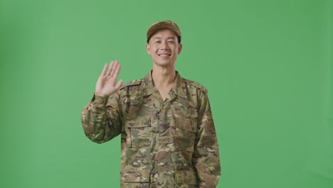 asian man soldier smiling, waving hand, and saying bye while standing in the green screen background studio