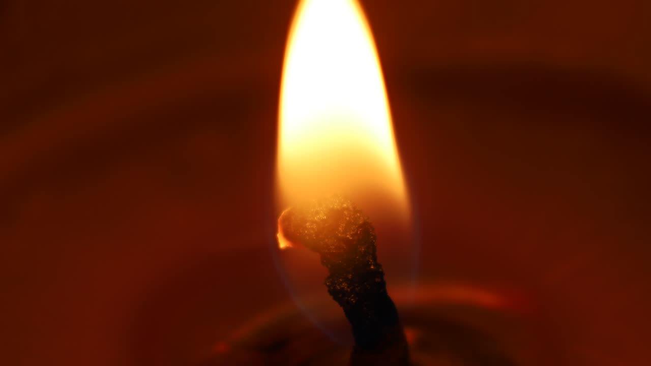 Single candle flame flickering in darkness, glowing softly with warm light