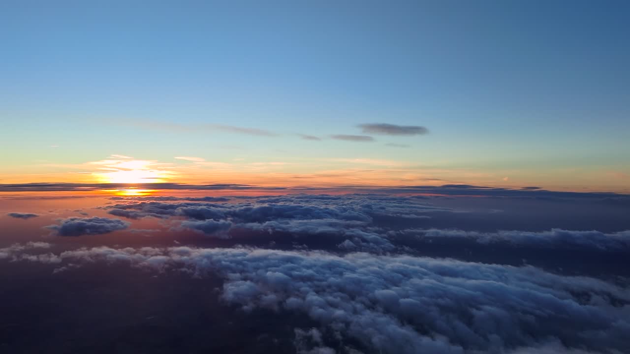 Pilot POV from cockpit while flying peacefully at the golden minute over a layer of broken clouds an the sun sinking beyond a golden horizon illuminating the clouds with pastel colors
