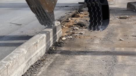 vista de cerca del cucharón de una excavadora agarrando y quitando el viejo borde de la acera para ensanchar la carretera