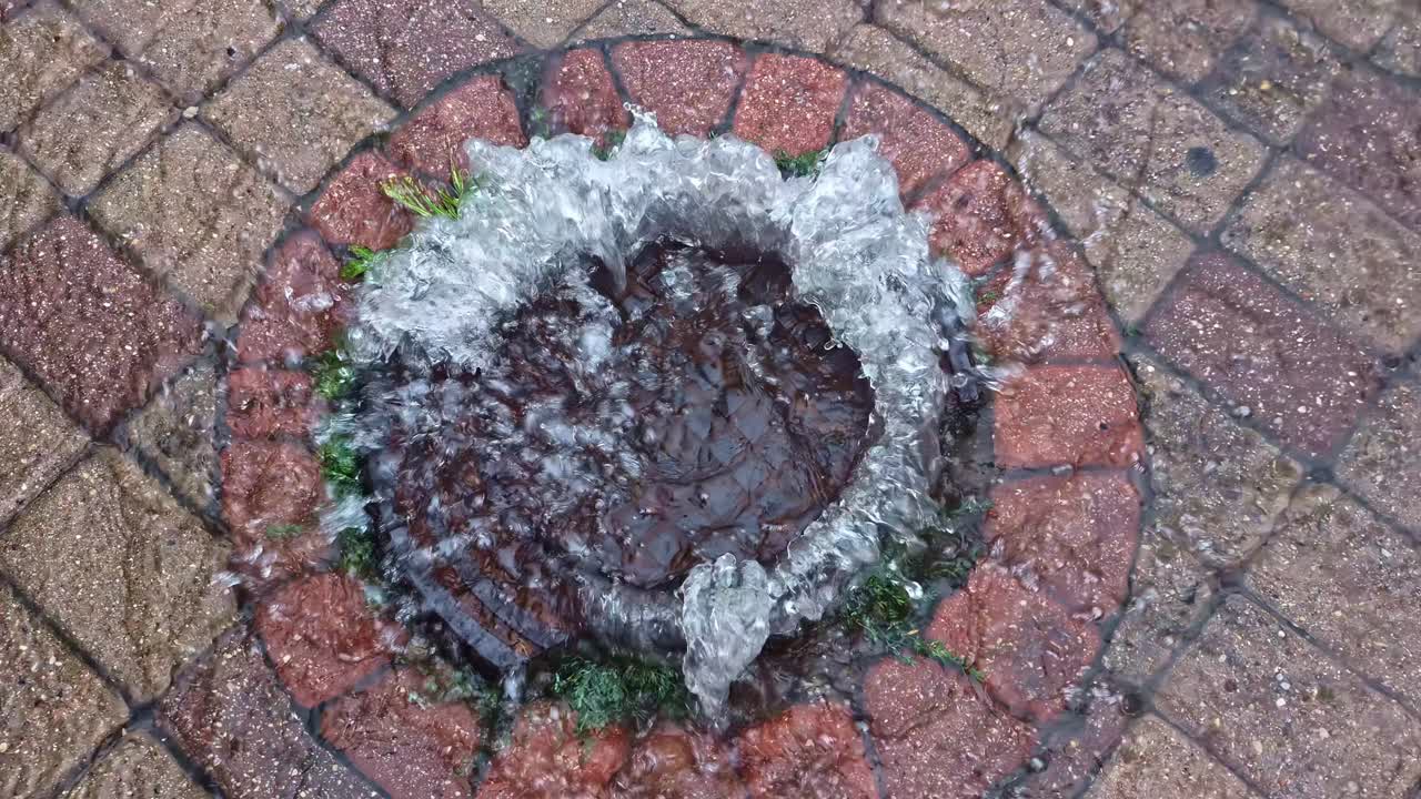 Gushing water through manhole on wet pavement after rainstorm