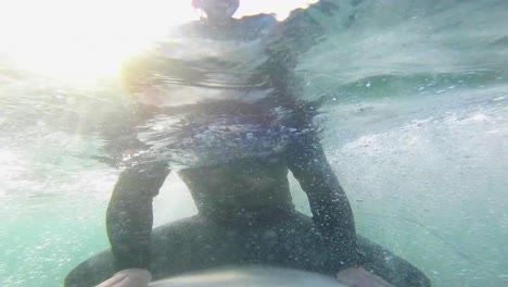 portrait of young surfer man with sun behind at sunrise on surfboard