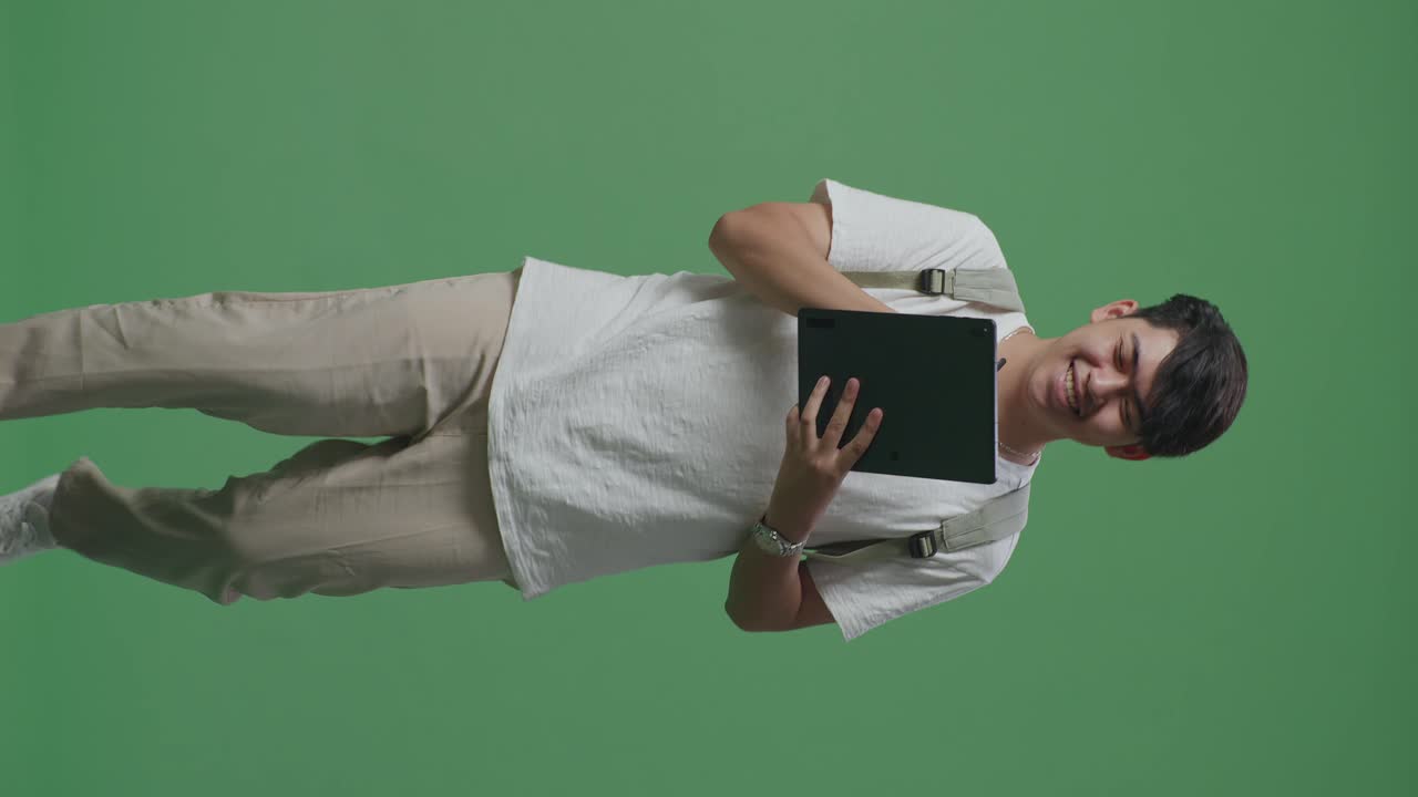 hombre asiático estudiante escribiendo en la tableta y caminando en el estudio de pantalla verde
