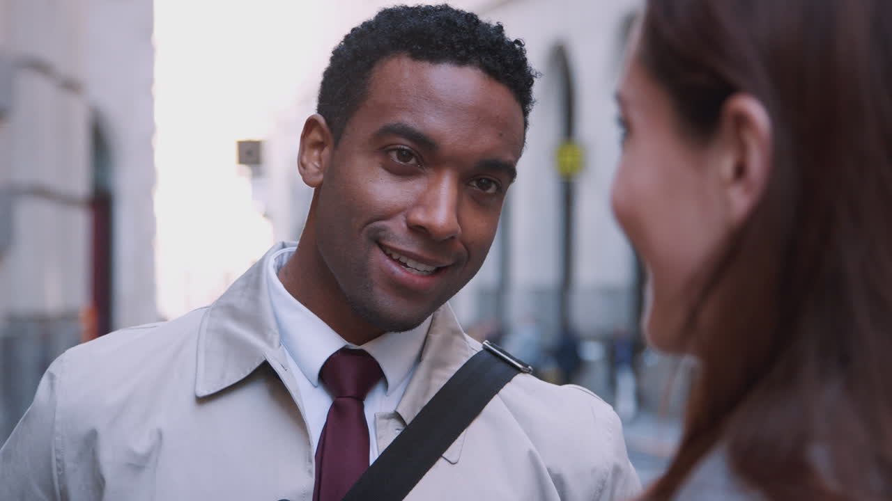 Millennial black businessman standing in the street listening his white female colleague talking, close up, selective focus