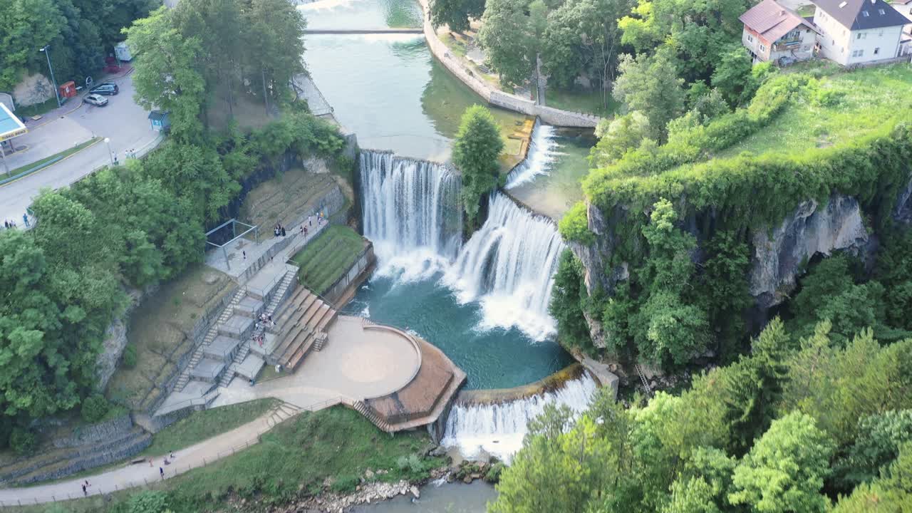 High aerial backward flight over river, city waterfall and park, Pocitelj