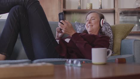Mujer-Usando-Auriculares-Usando-Un-Teléfono-Inteligente-En-Casa