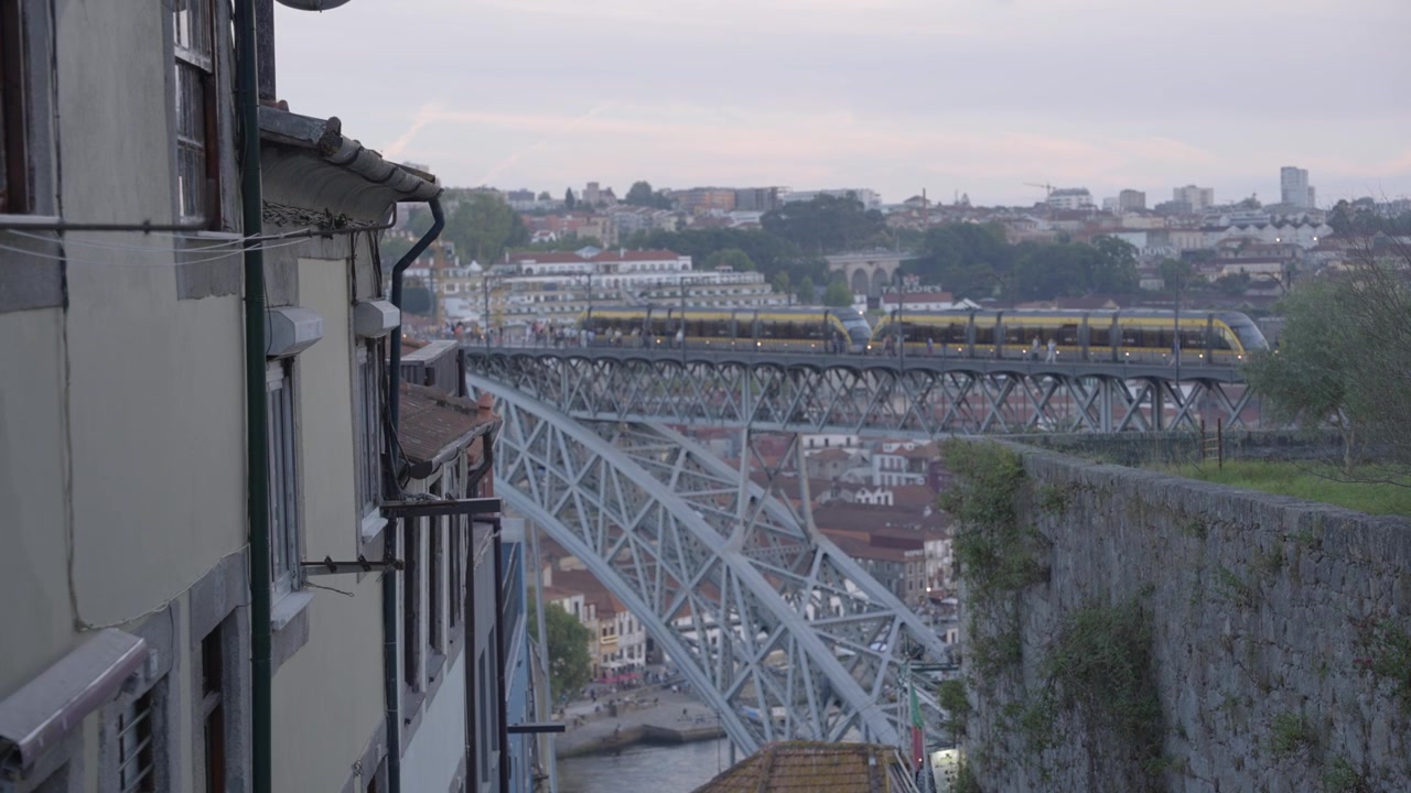 Treno elettrico e pendolari sul ponte Dom Luís I all'alba. Vista laterale incorniciata accanto a un edificio del centro storico. Ripreso in 4K a 25 fps