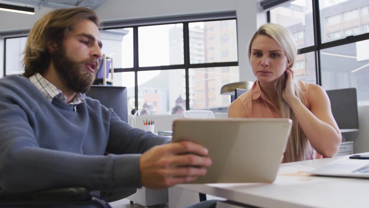Mand holder tablet og udløser RENDER- og PIXEL-etiketter, kvinde rækker ud efter bærbar computer og arbejder med design.