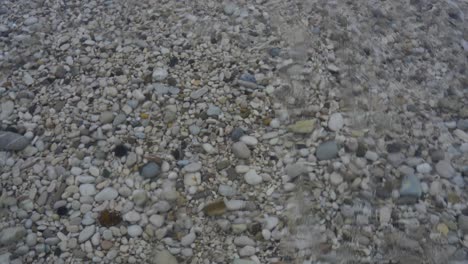 pebbles on shore wallow by clear crystal water of sea waves, seabed background for copy space