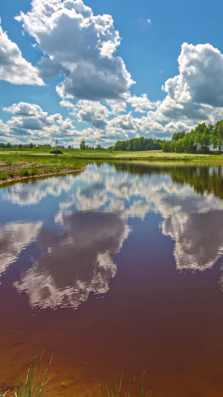 Vertical timelapse of fluffy clouds moving across the sky and reflecting in a calm river surface