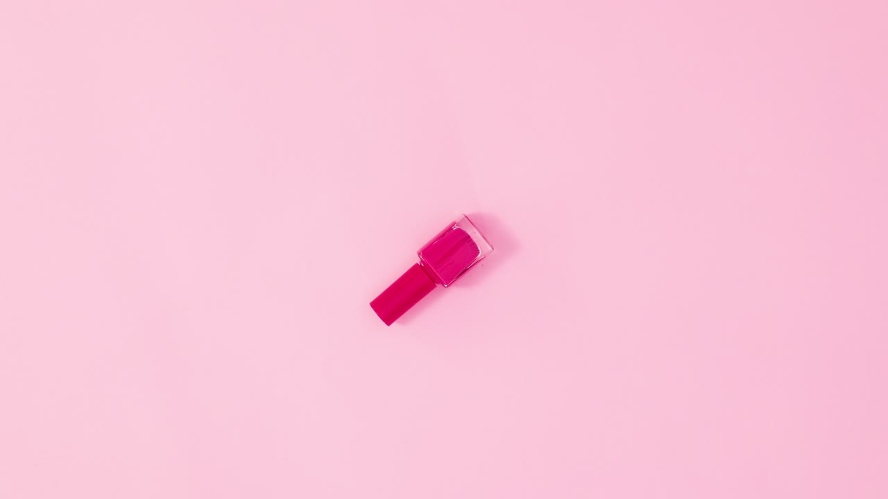 botella de esmalte de uñas de manicura girando sobre un fondo rosa pastel. colocación plana de movimiento de parada
