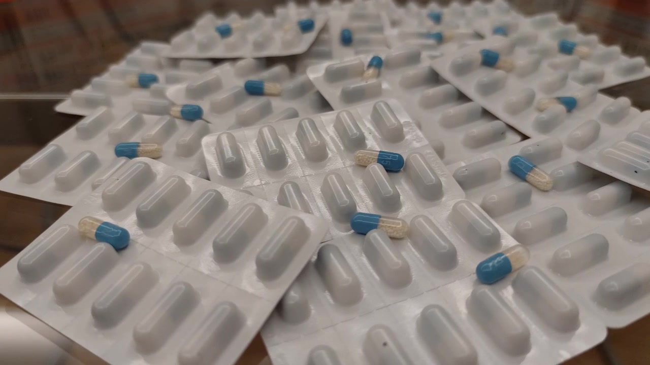 Pila di blister di medicinali blu e bianchi su tavolo di vetro