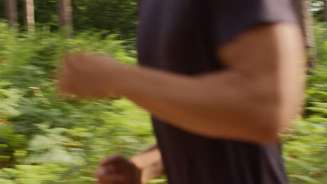 close up of man exercising doing work out outdoors running along track through forest past camera wearing sports clothing