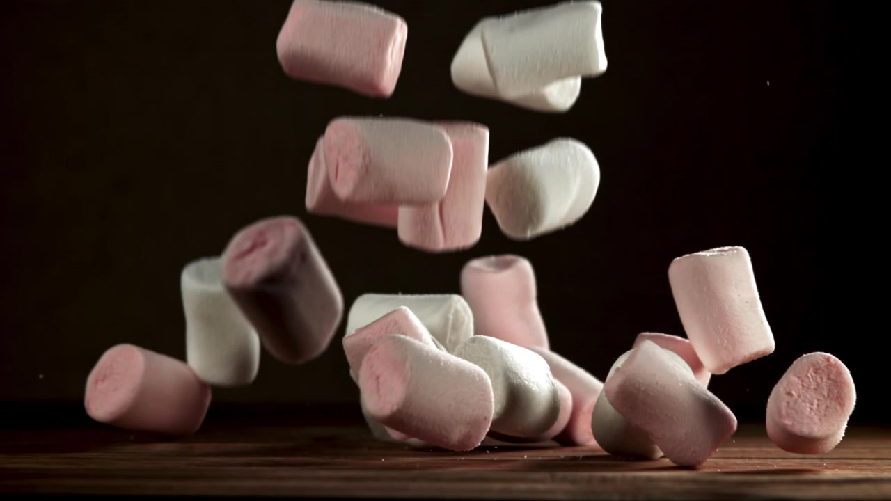 Marshmallow rosa e bianchi che cadono su una superficie di legno al rallentatore