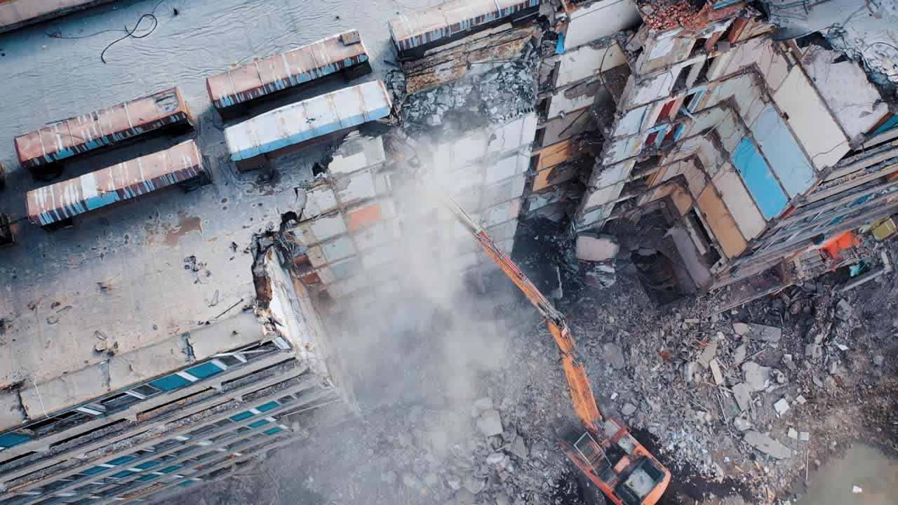 Destruction of an old multi-storey building by a machine. Work of the excavator at the construction site. A cloud of dust from destruction