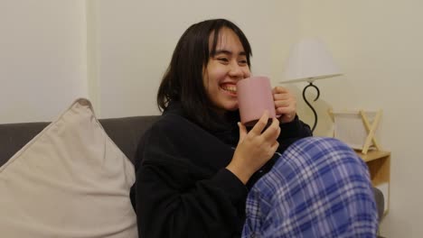 happy girl drinking coffee while watching tv on the sofa - close up