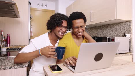 a happy gay couple using a laptop in the kitchen