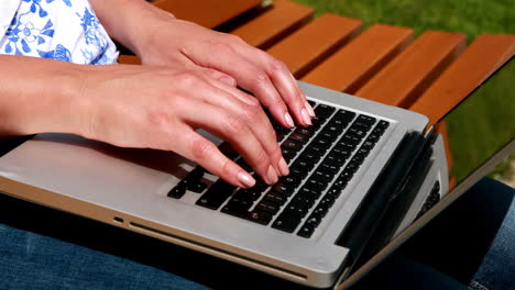 Woman sitting on park bench using laptop
