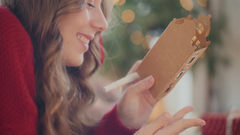 happy woman drawing outline on cardboard house during christmas at home