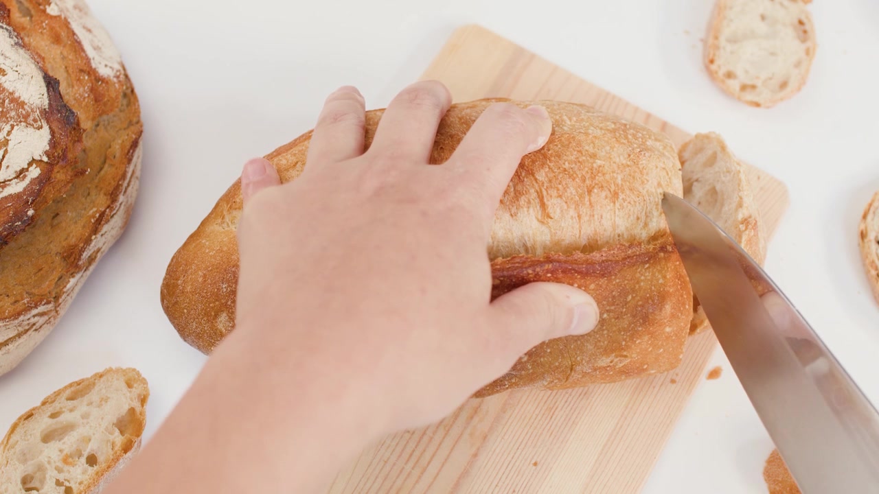 Ripresa dall'alto di mani che usano un coltello per affettare pane a lievitazione naturale biologico su sfondo bianco