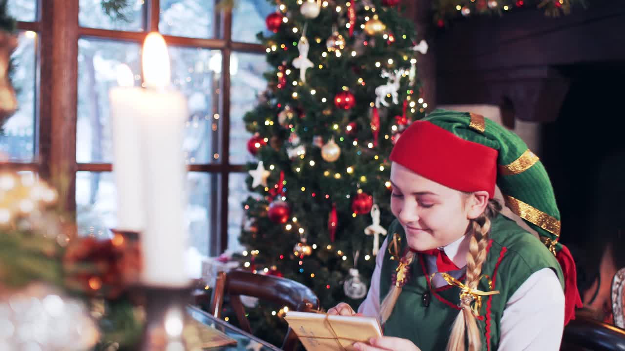 Cheerful girl elf looks through letters to Santa Claus. Room with a Christmas tree and candles