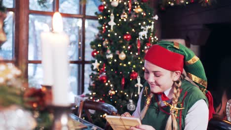 cheerful girl elf looks through letters to santa claus. room with a christmas tree and candles