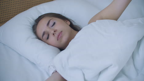 young woman wakes up in bed in the morning smiling raises her hands