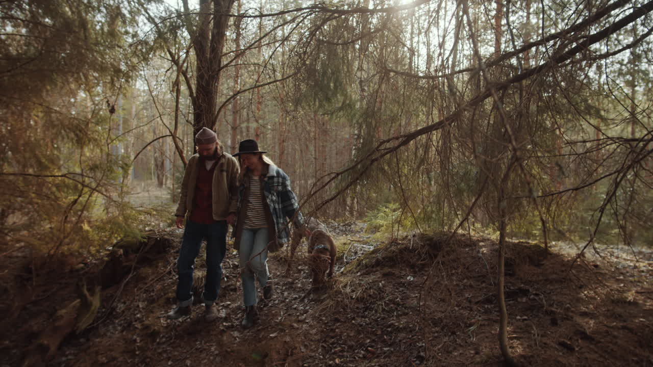 Couple Holding Hands and Walking with Dog in Woods