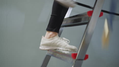 woman with bucket of paint climbs up step ladder in room