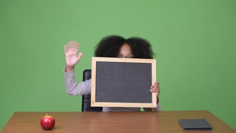 young cute african girl with afro hair showing blackboard while sitting