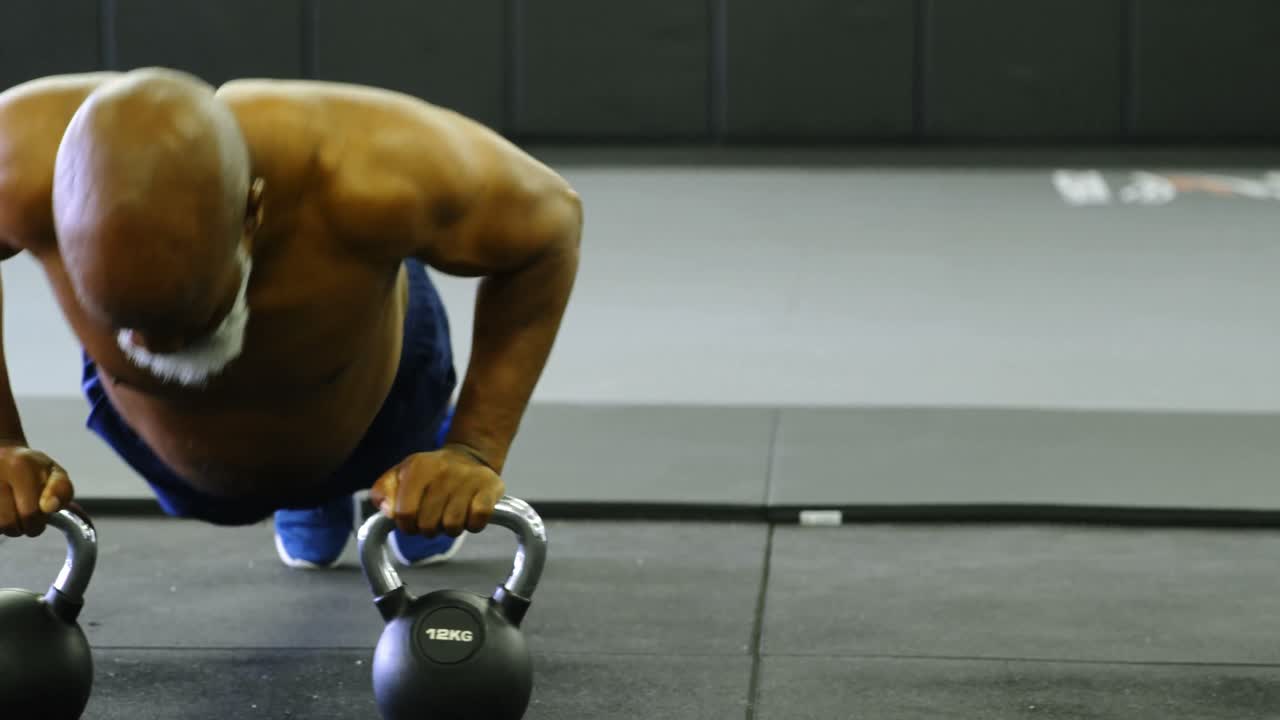 피트니스 스튜디오 4k 에서 케틀벨 과 함께 푸시업 을 하는 고령 남자