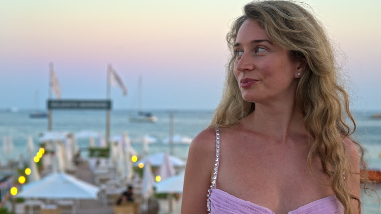Woman in pink dress posing with the beach on the background in the evening in Cannes, France