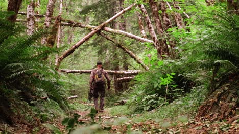 cazador masculino con un arco camina por el bosque verde