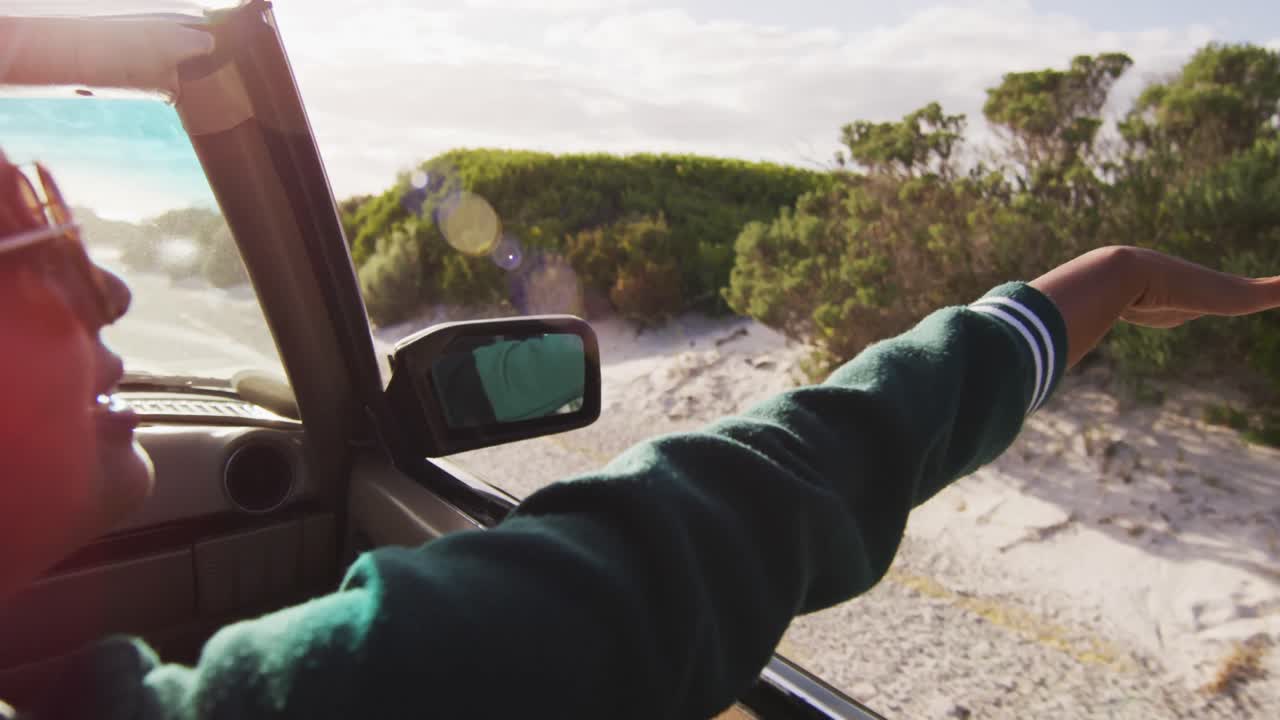 혼성 인종의 여성이  ⁇ 은 날 카브리톨 자동차를 운전하며 팔을 흔들고 미소 짓고 있습니다.