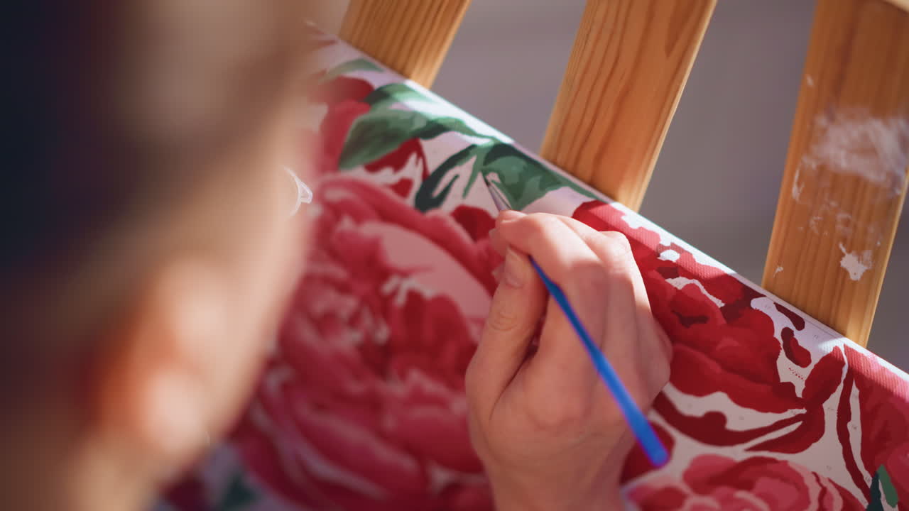 Close Detail Of Brush Working Across Patterned Fabric, Caucasian Artist Applies Careful Red And Green Strokes Near Easel, Steady Hand And Focused Studio Practice Create Textured Decorative Motif