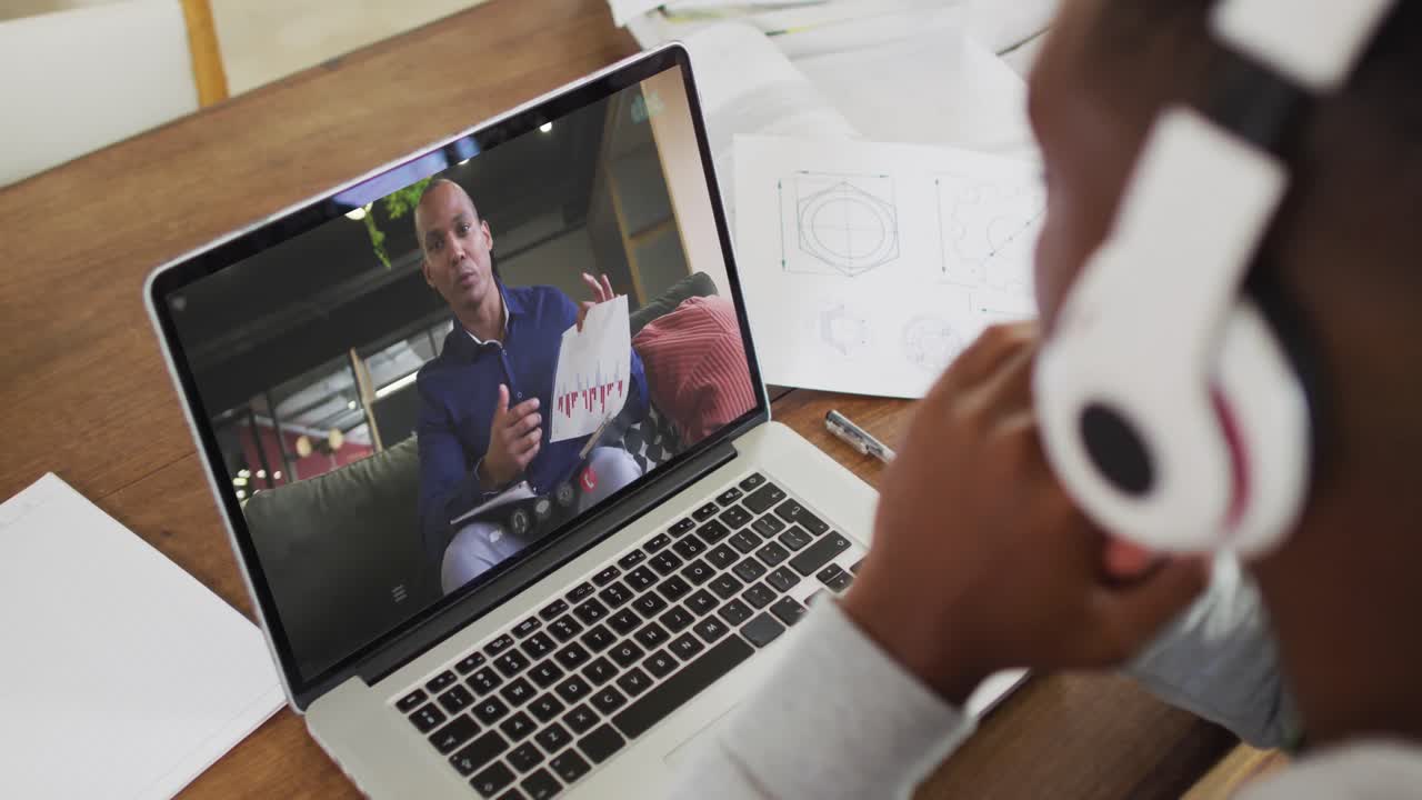 African american male college student wearing headphones having a video call on laptop at home