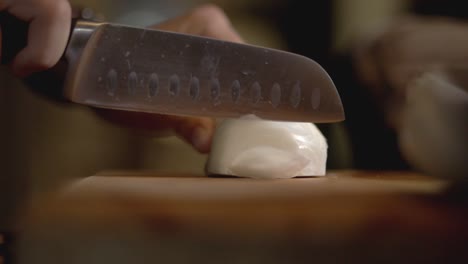 person using a stainless kitchen knife on cutting a white onion