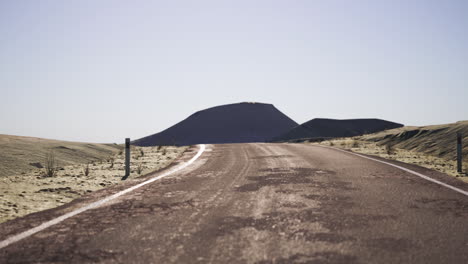 a long, empty road stretches out through a desert landscape, leading toward a mountain in the distance.