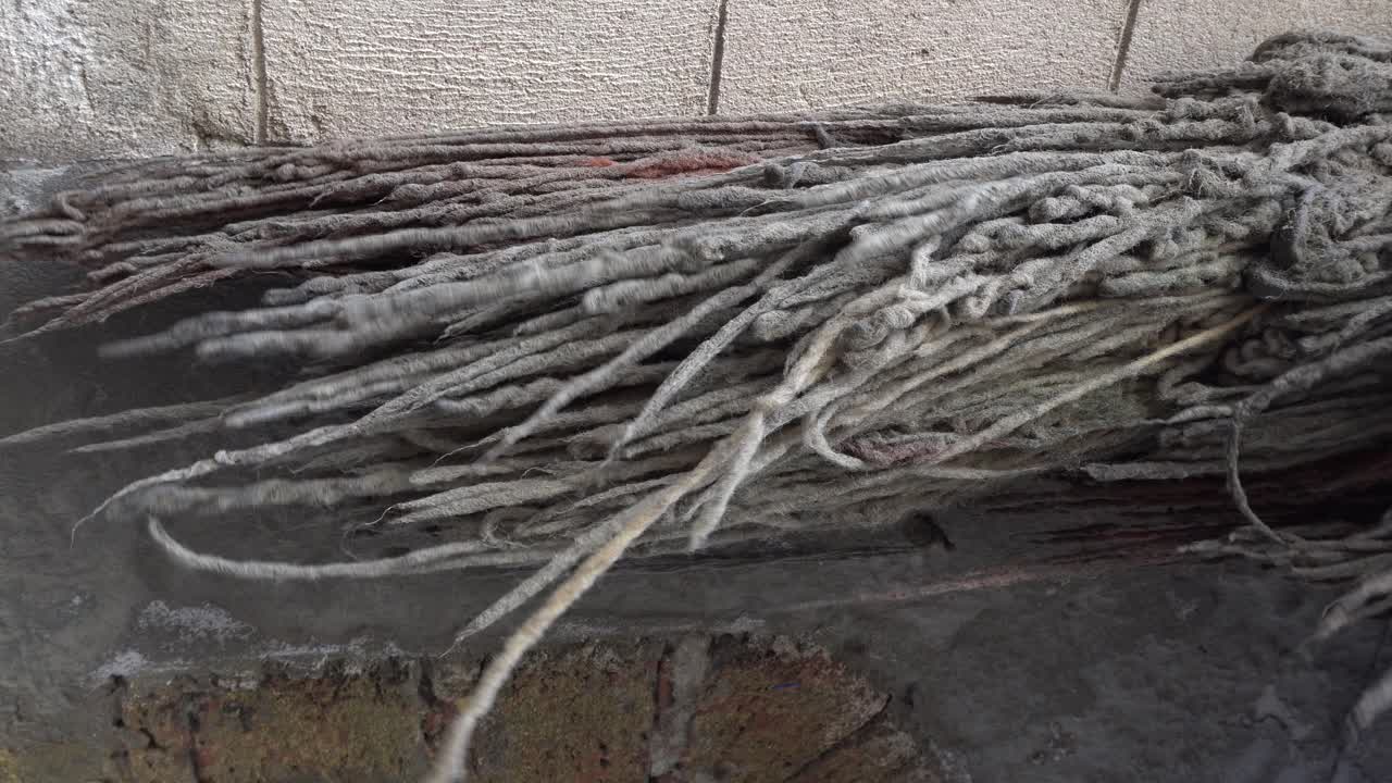 A bundle of white rope moves with the wind behind a brick wall