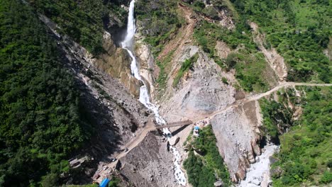 rupse falls and off-road suv cars drive on steep rough mountain dirt road in central nepal during summer day - aerial pull back reveal