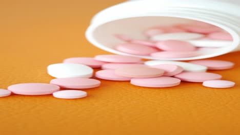 closeup of pink and white pills spilling out of a white bottle