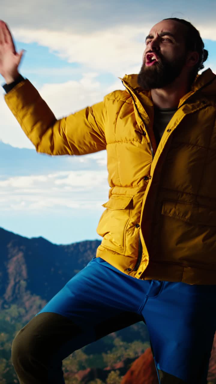 Uomo energico con giacca gialla che balla e salta in montagna