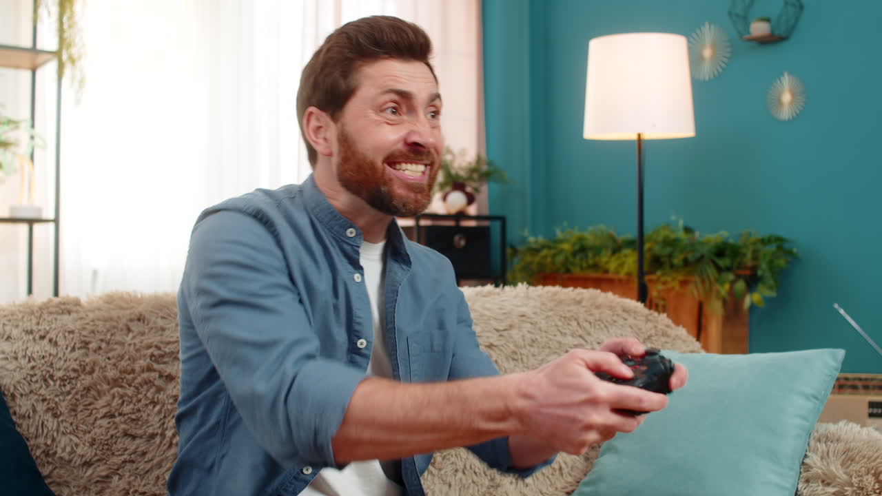 Young man intensely playing video game holding gamepad focused excited reacting home indoors sofa