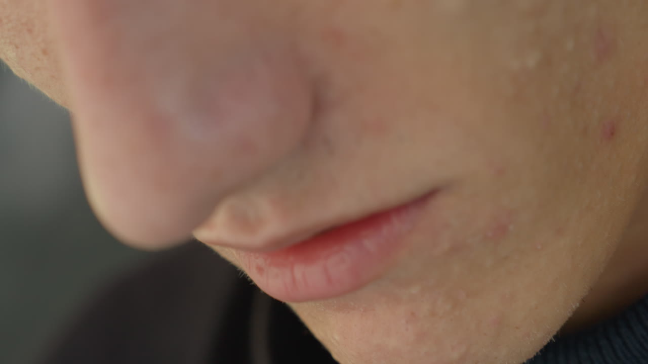 primo piano di un uomo caucasico che muove le labbra mentre parla, sussurro e respiro leggeri, pelle con texture e imperfezioni visibili, espressione pensierosa e profilo della mascella, attore che pronuncia una confessione silenziosa, atmosfera cinematografica intima