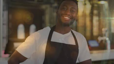 spots of light against portrait of male barista wearing apron smiling at cafe