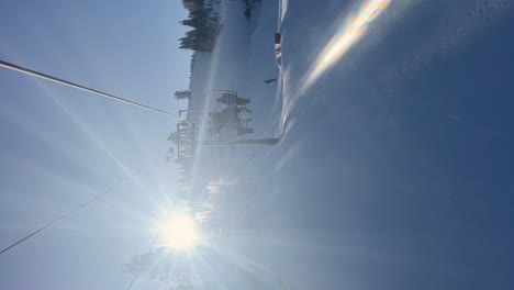 Vertikale-Handaufnahme-Nach-Oben-Kippen-Beim-Fahren-Auf-Einem-Langsamen-Skilift-In-Den-Rocky-Mountains-Von-Utah-An-Einem-Strahlend-Sonnigen-Wintertag-Mit-Einem-Kleinen-Eisenbahnpark-Darunter