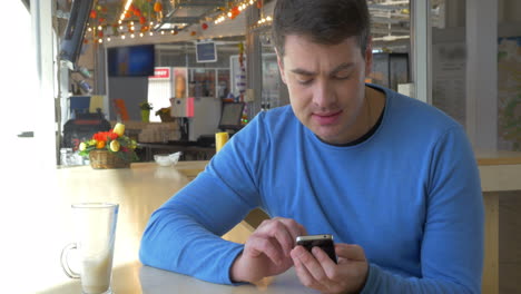 Hombre-Sentado-En-Una-Cafetería-Con-Un-Teléfono-Inteligente