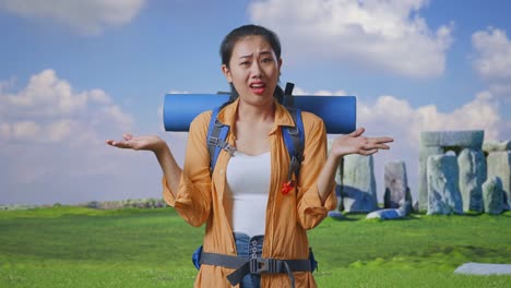puzzled asian female hiker with mountaineering backpack making gestures doubtfully and saying why while traveling in stonehenge