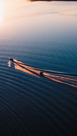 motor boat on water at sunset. panoramic view of the evening river with two boats. motor boat pulling small boat with people. view from above. vertical video