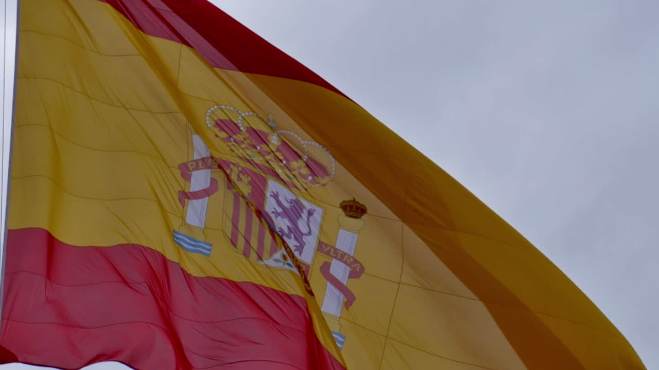 a Spanish flag waves proudly against a moody sky, its red and yellow colors vibrant and alive, evoking strength, heritage, and national identity.